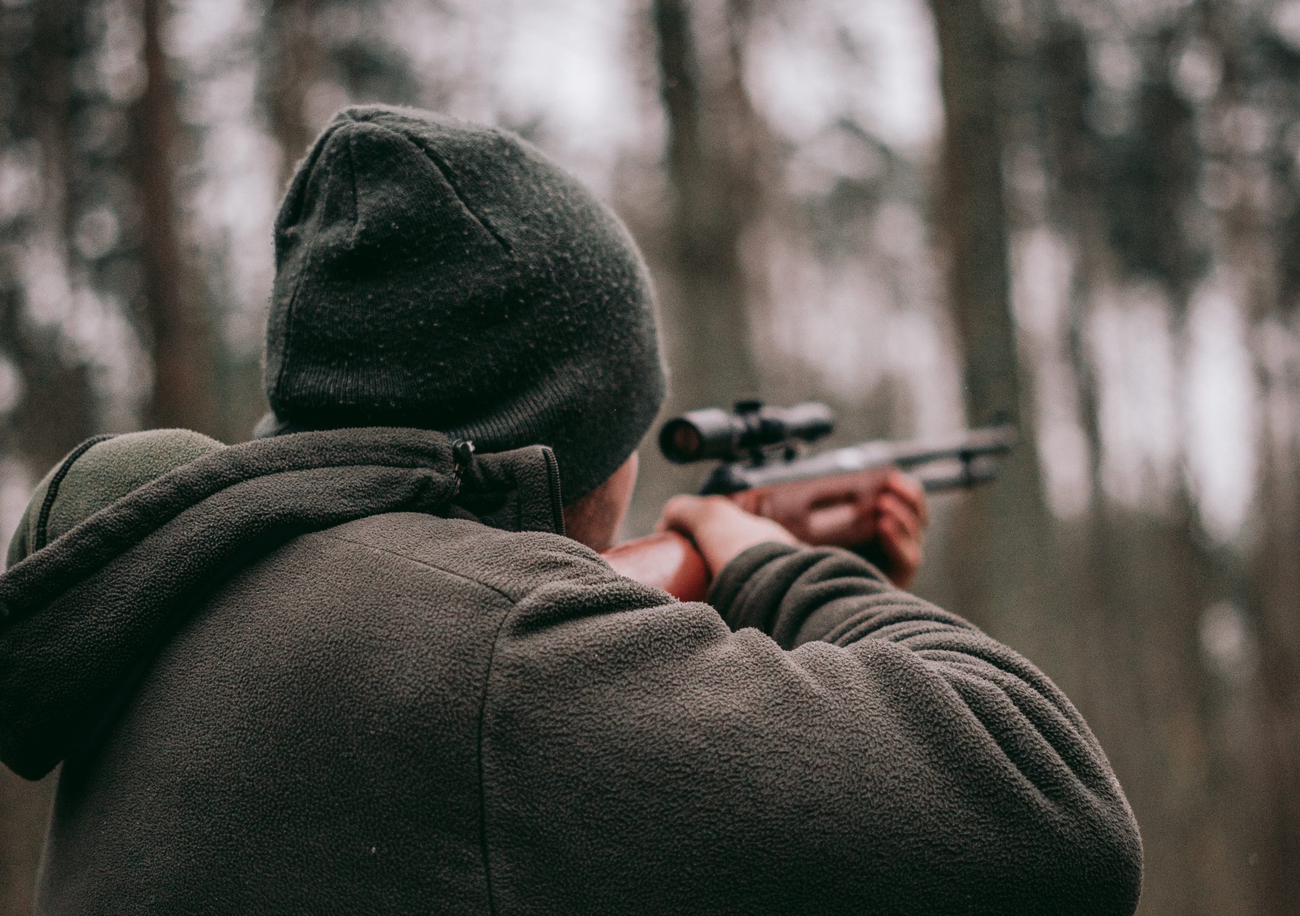 A man in a sweatshirt and a beanie shoots a gun.