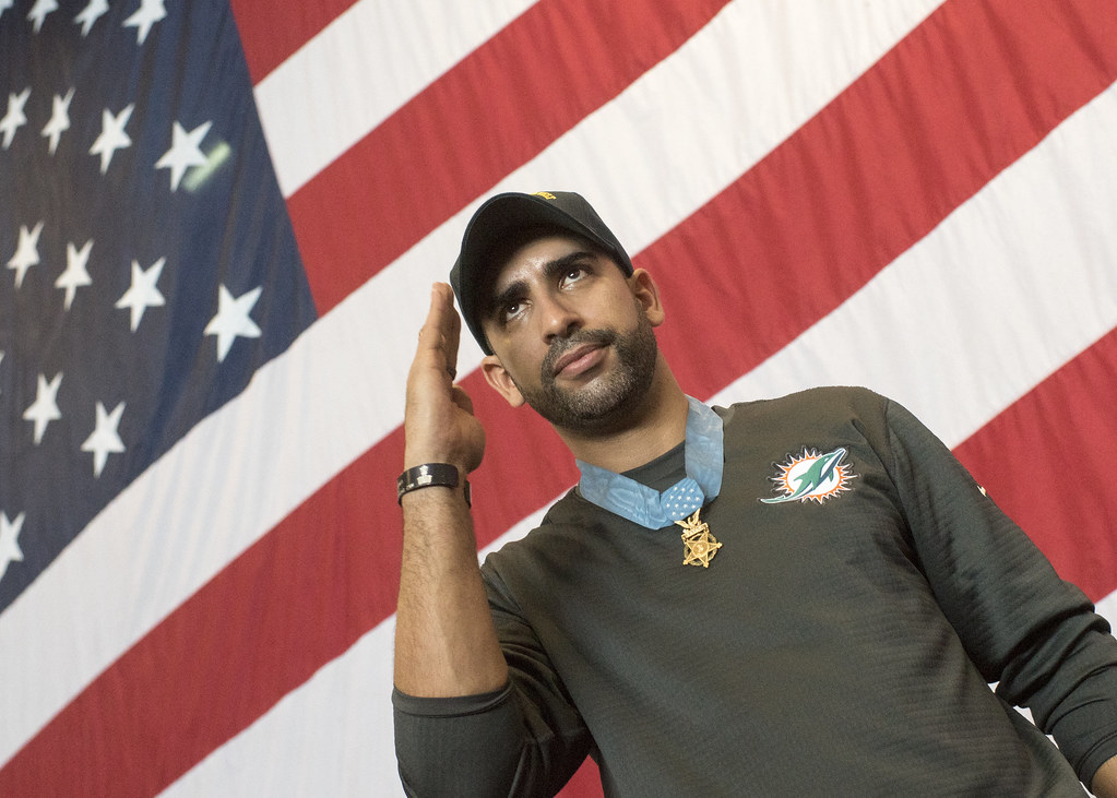 Florent Groberg stands in front of a large American flag.