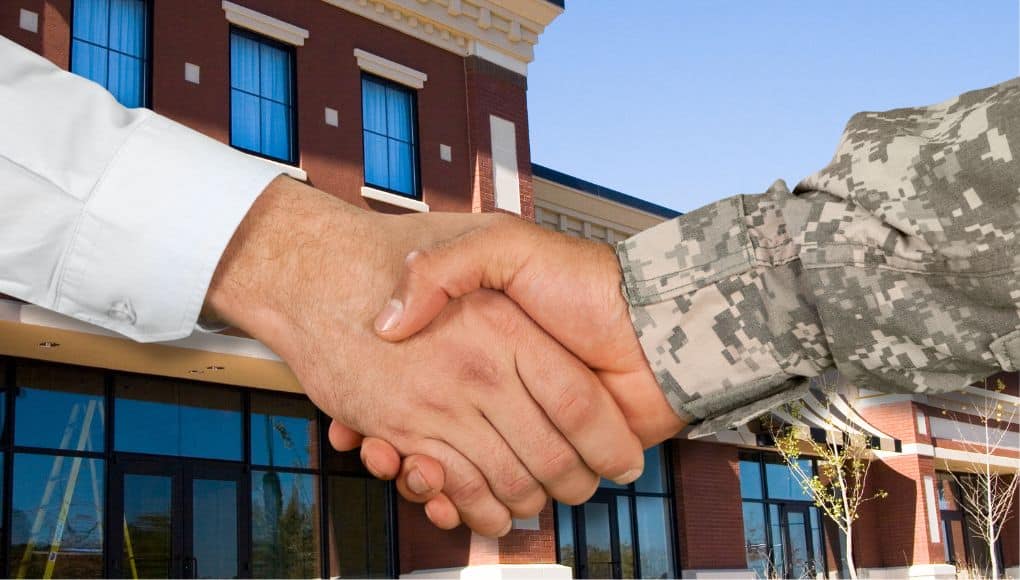 A close-up image of a handshake between someone wearing a dress shirt and someone wearing a military uniform.