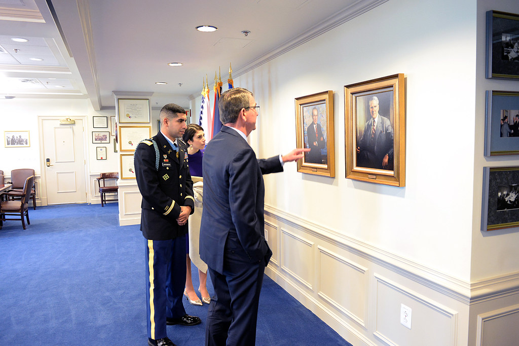 Florent Groberg stands beside a man in a suit. Both men are looking at a framed painting.