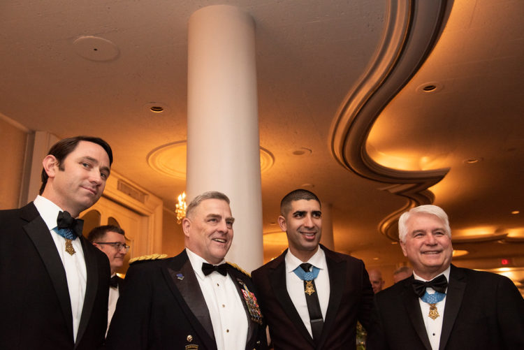 Florent Groberg stands beside three other men in suits.
