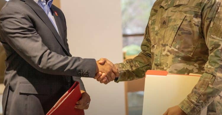 A close-up shot of a handshake between a person in a suit and a person in a military uniform.