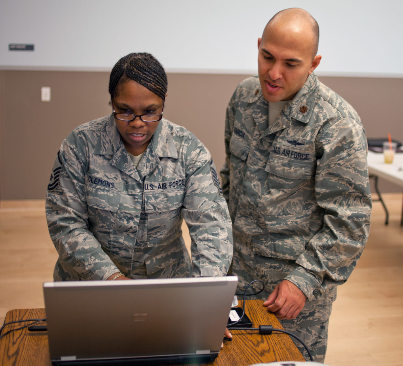 A man and a woman in military uniforms stand in front of a laptop computer.