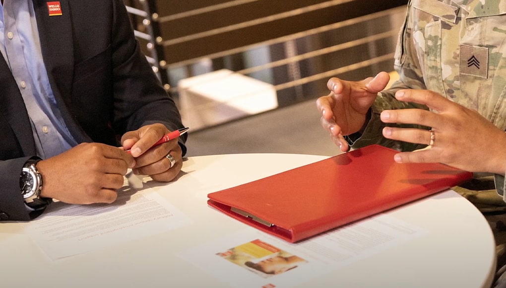 Red folder sits on a white table. Two people are sitting around the table, one of whom is in civilian clothing and the other is wearing a military uniform.