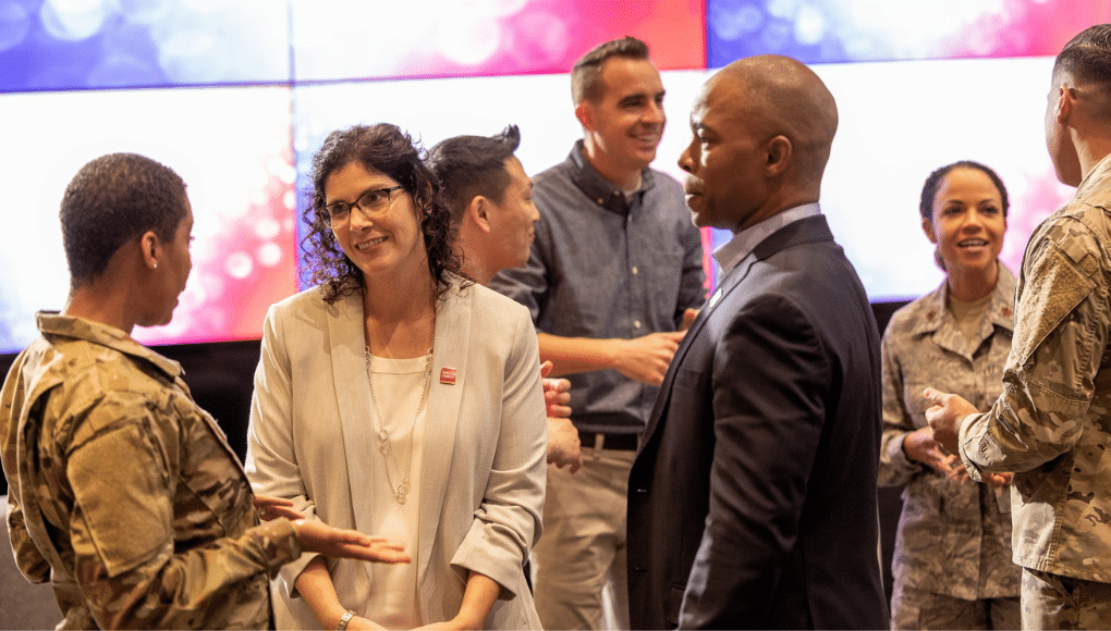 A group of people, some of whom are dressed in military fatigues and others dressed in suits, socialize together.